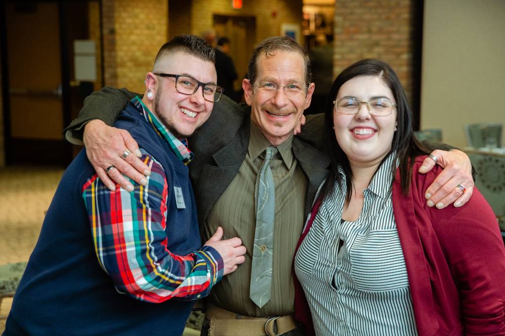 Three guests hugging and smiling at Scholarship Dinner 2019